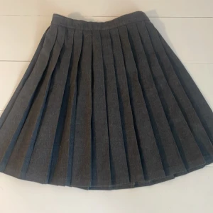 Grå plisserad kjol - Snygg grå plisserad kortkjol med klassiska veck. Kjolen har en enkel och stilren look. Midjan är lätt elastisk för extra komfort. Använd endast ett fåtal gånger. Ser ny ut utan tecken på användning. 