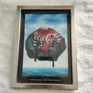 Coca Cola on the Rocks - Cool och unik konstbild av Paul Riesser, där en smältande Coca Cola-burk svävar över havet. Perfekt för dig som gillar popkultur och vill ha något annorlunda på väggen. Inramad och redo att hängas upp – ett måste för unga konstälskare! Mått cirka 17 x 23 cm