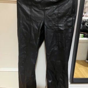 Svarta skinnbyxor med utsvängda ben - Snygga svarta byxor i skinnimitation med raka ben och diskreta sömmar längs framsidan. Perfekta för en edgy look och lätta att matcha med både sneakers och boots.