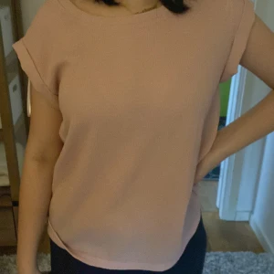 Ljusrosa blus med korta ärmar - Enkel och stilren ljusrosa blus med rund halsringning och uppvikta korta ärmar. Toppen har en lätt strukturerad yta och rak passform, perfekt för en clean och avslappnad look.