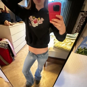 Svart Pink Panther hoodie med strass - Svart hoodie med Pink Panther-motiv i strass på bröstet. Tröjan har huva, lång ärm och en croppad passform som ger en cool och avslappnad vibe. Perfekt för dig som gillar statement-plagg 💕