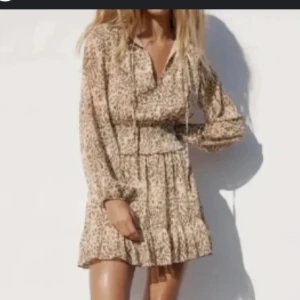 Beige leopardmönstrad kortklänning - Supersöt kortklänning i beige med leopardmönster och v-ringning. Klänningen har långa ärmar, volang nertill 