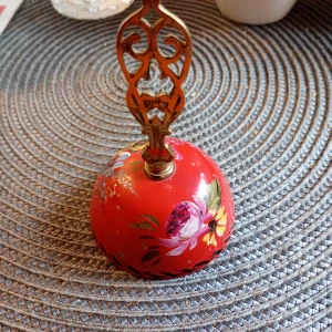 Vintage Bordsklocka röd med blommor och metall handtag  - Säljer en Bordsklocka i en unik, rund  av metall med handmålat blommönster i rött, blått och gult.handtaget har ett dekorativt handtag i mässing med snirkligt mönster. Perfekt för dig som gillar vintage och vill ha något annorlunda på bordet.