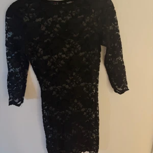 Svart spetsklänning med trekvartsärm - Snygg svart kortklänning i spets med trekvartsärm. Klänningen har en figurnära passform och är helspetsad.