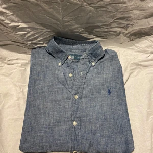 Ralph Lauren skjorta  - Snygg blå skjorta från Ralph Lauren i custom fit med klassisk button down-krage och broderad logga på bröstet. Skjortan är långärmad. Storlek M, hör av er vid frågor 