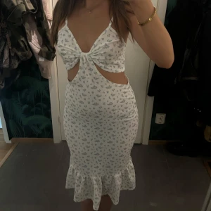 Vit blommig midiklänning  - Superfin vit klänning med små blå blommor, volangkant nertill och snygga cut-outs vid midjan. 