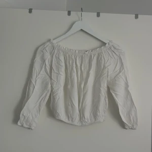 Vit offshoulder blus Brandy Melville - Supersöt vit blus från Brandy Melville med offshoulder-modell och långa ärmar. Blusen har resår vid halsringningen och ärmarna för en snygg rynkad effekt. Perfekt att styla med jeans eller kjol för en trendig look.