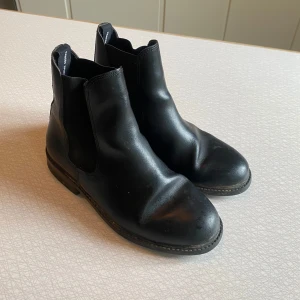 Svarta ridskor, jodhpurs,  från Hansbo Sport strl 36 - Klassiska svarta ridskor, jodhpurs, från Hansbo Sport i skinn med elastiska paneler på sidorna och dragflik bak. Snygg, tidlös design med låg klack och rund tå. Använda en timme i veckan under ca 2 säsonger. Lite skav på sulan, men annars bra skick! Strl 36 med stålhetta. Nypris ca 800kr