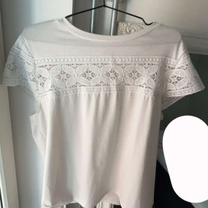 Vit tröja med spetsdetaljer - Superfin vit tröja med korta ärmar och breda spetsinslag över axlar och bröst. Tröjan har rund halsringning och ett mjukt, lätt tyg som känns skönt mot huden. Perfekt för dig som gillar romantiska detaljer och en clean look.