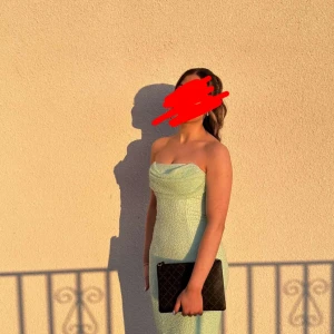 Oh polly klänning  - Säljer en elegant ljusgrön långklänning med axelbandslös design och figurnära passform. Klänningen har en glittrig yta och en snygg drapering vid bysten. Perfekt för bal eller festliga tillfällen. Materialet känns lyxigt och skimrar fint i ljuset.