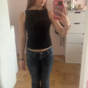 Svart glittrig ärmlös topp - Säljer en svart ärmlös topp med glittriga små paljetter över hela tyget. Toppen är croppad och har en slim passform som sitter snyggt mot kroppen. Perfekt för dig som vill sticka ut lite extra med en enkel men ändå festlig look.