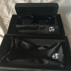 All cap one solglasögon blue shades.  - Snygga svarta glasögon från All Cap One med rund form och diskreta silvriga detaljer vid bågfästena. Kommer med matchande svart fodral och putsduk med logga. Perfekta för dig som vill ha en stilren och modern look. Hör av dig om de skulle va några frågor!
