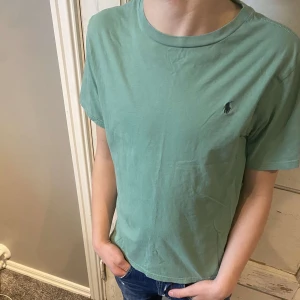 Grön t-shirt från Ralph Lauren - Säljer en stilren grön t-shirt från Ralph Lauren med den klassiska loggan broderad på bröstet. T-shirten är kortärmad och gjord i mjuk bomull. Perfekt för en avslappnad look. Priset är ej hugget i sten, hör av dig vid funderingar!