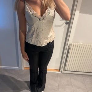 Vit spetsprydd linnetopp - Säljer en stilren vit linnetopp med vacker spetsdetalj vid urringningen. Toppen har smala axelband och en figurnära passform som framhäver silhuetten. Perfekt för en elegant look. (Väldigt skrynklig i bilden men den går såklart att stryka) 