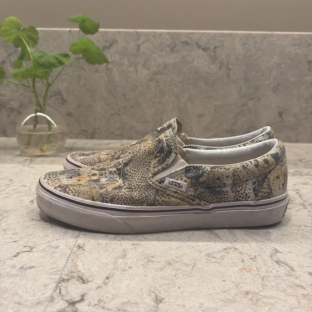 Snygga slip-on sneakers från Vans med ett coolt leopardmönster. Skorna har en bekväm passform och är perfekta för en avslappnad stil. De har en vit sula som kontrasterar snyggt mot det djärva mönstret.. Kengät.
