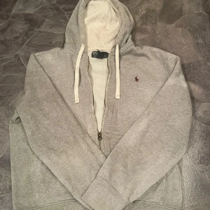 Grå hoodie från Polo Ralph Lauren - Säljer en stilren grå hoodie från Polo Ralph Lauren med dragkedja och klassisk logga på bröstet. Sitter som m ungefär skulle jag säga!