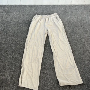 Beige byxor från Lindex - Säljer ett par bekväma beige linnebyxor från Lindex. De har en elastisk midja och är tillverkade i ett lätt material, perfekt för en avslappnad stil. Byxorna har en rak passform och är idealiska för vardagsbruk.