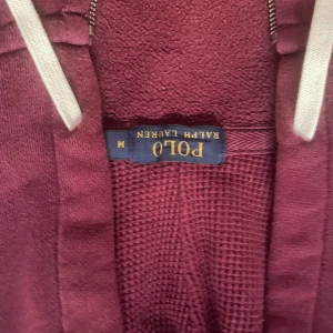 Vinröd hoodie från Polo Ralph Lauren - Säljer en snygg vinröd hoodie från Polo Ralph Lauren. Den har en dragkedja framtill och en praktisk huva med vita snören. Perfekt för en avslappnad stil.