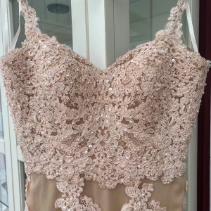 Champagnefärgad långklänning med spetsdetaljer i ljusrosa - Elegant långklänning/balkläning i champagnefärg med vackra spetsdetaljer och smala axelband. Klänningen har en figurnära passform och är dekorerad med blommönster i spets över hela tyget. Klänningen har även en djup rygg som göra ty klänningen börjar i mitten av ryggen. Perfekt för en speciell kväll!! Klänningen passar alla mellan xs till s jag själv har storlek XS, S samt kan ha M och klänningen passar perfekt på mig. Pris går att diskuteras och fler bilder fins vid intresse. ✨🌸