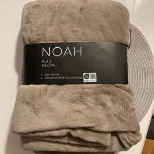 Beige pläd från NOAH - Mysig beige pläd från NOAH i storleken 130x150 cm. Tillverkad av 100% polyester och certifierad enligt OEKO-TEX standard 100. Perfekt för att hålla sig varm och bekväm hemma. Finns 2 stycken, 220kr styck eller 400kr för båda