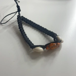 Svart armband med sköldpadda och snäckor - Unikt handgjort svart armband med en orange sköldpadda och vita snäckor. Perfekt för en bohemisk stil eller sommarens stranddagar. Justerbar passform med flätad design.