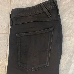 Svarta jeans från Replay - Snygga svarta jeans från Replay med klassisk femficksdesign och knappgylf. De har en stilren look med diskreta sömmar och en liten logga på bakfickan. Perfekta för en stilren vardagslook.