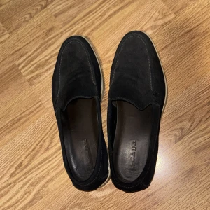 Mörkblåa loafers i mocka - Snygga mörkblåa loafers i mocka med en stilren design. Skorna har en vit sula som ger en fin kontrast till det svarta. Perfekta för en avslappnad men ändå elegant look. Märket är Massimo dutti och dessa skor är knappt använda. Priset går att diskutera. 