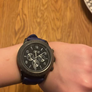 Blå klocka från One - Snygg klocka från One med blått armband och svart urtavla. Klockan har en stilren design med flera små urtavlor och tydliga siffror. Perfekt för dig som vill ha en modern accessoar inte så använd och bra pris obs behövs nytt batteri.