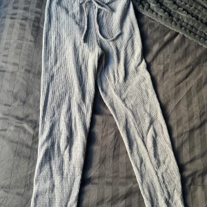 Grå ribbade byxor från Bohemian - Snygga grå ribbade byxor från Bohemian i mjukt och bekvämt polyester. Aldrig använda av mig då dem är för små men jag köpte dom begagnade. Finns ett litet hål på ena benet, annars i bra skick. 