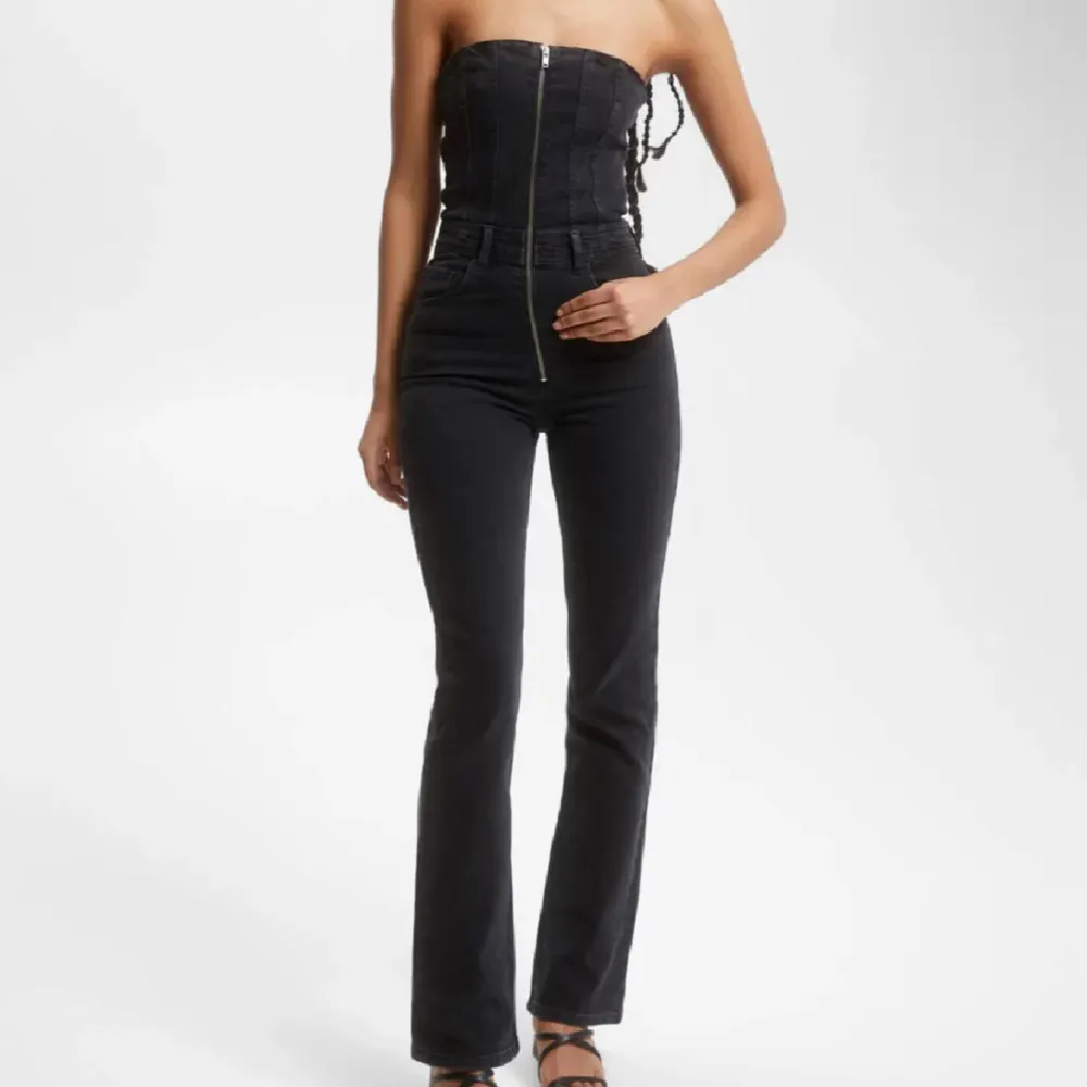 Trendig svart jumpsuit med en tight passform. Den har en dragkedja framtill som ger en snygg detalj. 300kr+frakt. Farkut & Housut.