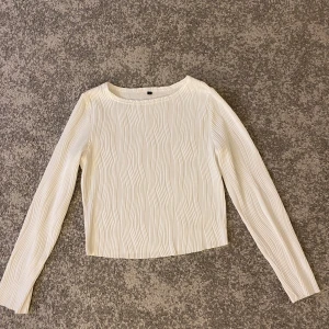 Vit långärmad topp med textur - Säljer en stilren vit topp med lång ärm och en unik textur. Perfekt för att ge en elegant touch till din outfit. Toppen har en rund halsringning och är i storlek M.