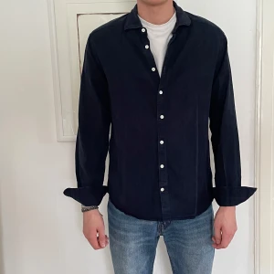 Mörkblå J.Lindeberg skjorta - Snygg mörkblå långärmad J.Lindeberg skjorta med klassisk krage och knappar framtill. Perfekt med jeans eller linnebyxor! Står storlek L, men sitter som en M. 