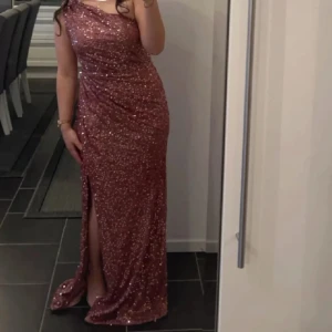 Balklänning - Säljer en fantastisk rosa långklänning med glittrande paljetter. Klänningen har en elegant oneshoulder-design och en slits som ger en extra touch av glamour. Perfekt för en speciell kväll! Har endast använts en gång!! Kemtvätt. Pris går att diskuteras. 
