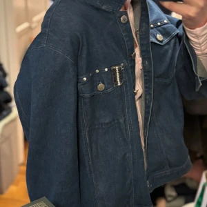 Blå jeansjacka med detaljer - Snygg blå jeansjacka med knappar och coola detaljer på bröstfickorna. Jackan har en normal passform och långa ärmar. Perfekt för en avslappnad stil.