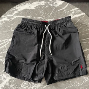 Ralph Lauren Badbyxor  - Snygga svarat badshorts från Ralph Lauren. De är använda få gånger däremot har de en liten defekt som kan ses på bild 4. Stygnen råka gå sönder men sydde ihop den och syns absolut ingenting, till och med lite svårt att se på bilden. De är storlek XL men passar inte särkilt bra för XL och skulle passa bättre på M. Vid några övriga frågor är det bara att höra av dig.  MVH Stockholm Wardrobe😄