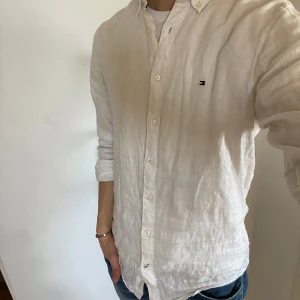 Linneskjorta - Säljer en vit linneskjorta från Tommy Hilfiger. Skjortan har långa ärmar och knappar framtill. Perfekt för en avslappnad men ändå elegant look. Den är tillverkad i premium linne vilket ger en skön och luftig känsla. Den är i storlek s och skick är 7,5/10. Den har en liten skada på bröstet men ej något som man märker tydligt! Hör av er vid vidare funderingar eller frågor🙌
