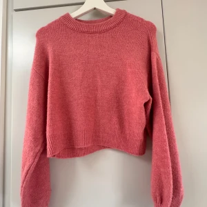 Rosa stickad tröja från NA-KD - Säljer en snygg rosa stickad tröja från NA-KD. Tröjan är croppad med långa ärmar och har en ribbad kant vid halsen och ärmsluten. Perfekt för en stilren och bekväm look.