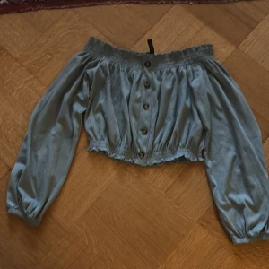 Grön offshoulder blus med knappar - Säljer en söt grön offshoulder blus med knappar framtill. Blusen har långa ärmar och en elastisk kant vid axlar och midja för en bekväm passform. Perfekt för en avslappnad stil.