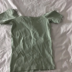 Grön offshoulder topp från Gina Tricot - Säljer en stilren grön offshoulder topp från Gina Tricot. Perfekt för varma dagar med sin lätta och bekväma passform. Toppen har korta ärmar och är gjord i mjukt bomullsmaterial.