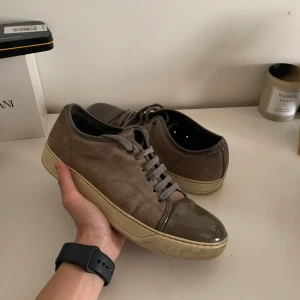Lanvin skor - Snygga grå sneakers från Lanvin med en kombination av mocka och glansigt material på tån. Skorna har en klassisk snörning och en bekväm sula. Perfekta för en stilren look. Skick 9/10, inga synliga slitningar✅ Färg brun, storlek 40. Dem ser mycket bättre ut i verkligheten, Box/Dustbag kommer inte med 