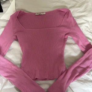 Rosa ribbad topp från NA-KD - Säljer en rosa långärmad ribbad topp från NA-KD med fyrkantig ringning. Toppens material är stretchigt och sitter figurnära. Perfekt att styla med jeans eller kjol. Endast en defekt på lappen på insidan som syns på bilden. 