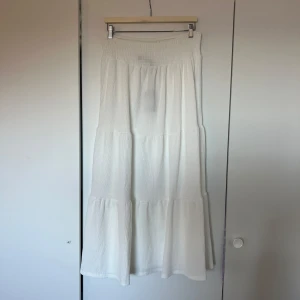 Vit långkjol - Säljer en vit långkjol med bred resår i midjan. Kjolen har en luftig och flowy känsla, perfekt för varma dagar. Enkel att matcha med olika toppar för en avslappnad stil. Den är i väldigt bra skick då lappen fortfarande sitter kvar!✨🫧🩷