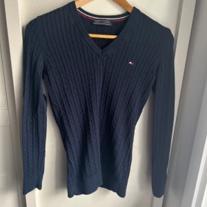 Mörkblå kabelstickad tröja från Tommy Hilfiger - Jätte fin tröja med en v neck, storleken L men sitter även fint på mig som är storlek xs/s, ger en snatched look 