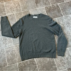 Olivlgrön stickad tröja från Samsøe Samsøe -  Olivgrön stickad tröja från Samsøe Samsøe med rund halsringning och ribbade muddar vid ärmslut och nederkant. Tillverkad i en mjuk ull- och polyamidblandning som passar perfekt för kyligare vårkvällar. Vid minsta fråga så är det bara att kontakta! Pris ej fast i sten 🪨!