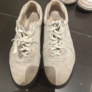 Ljusgrå sneakers från Axel Arigato - Snygga ljusgrå sneakers från Axel Arigato i mocka med svarta sulor. Skorna har snörning och en stilren design med rund tå. Perfekta för dig som gillar minimalistisk stil och vill ha något som funkar till det mesta.