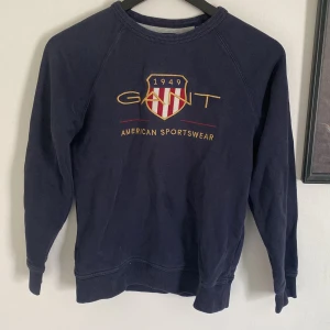 Mörkblå sweatshirt från Gant - Säljer en mörkblå sweatshirt från Gant med broderad logga och texten 'American Sportswear' framtill. Tröjan har rund halsringning och långa ärmar. Klassisk och stilren design med ribbade muddar vid ärmslut och nederkant.