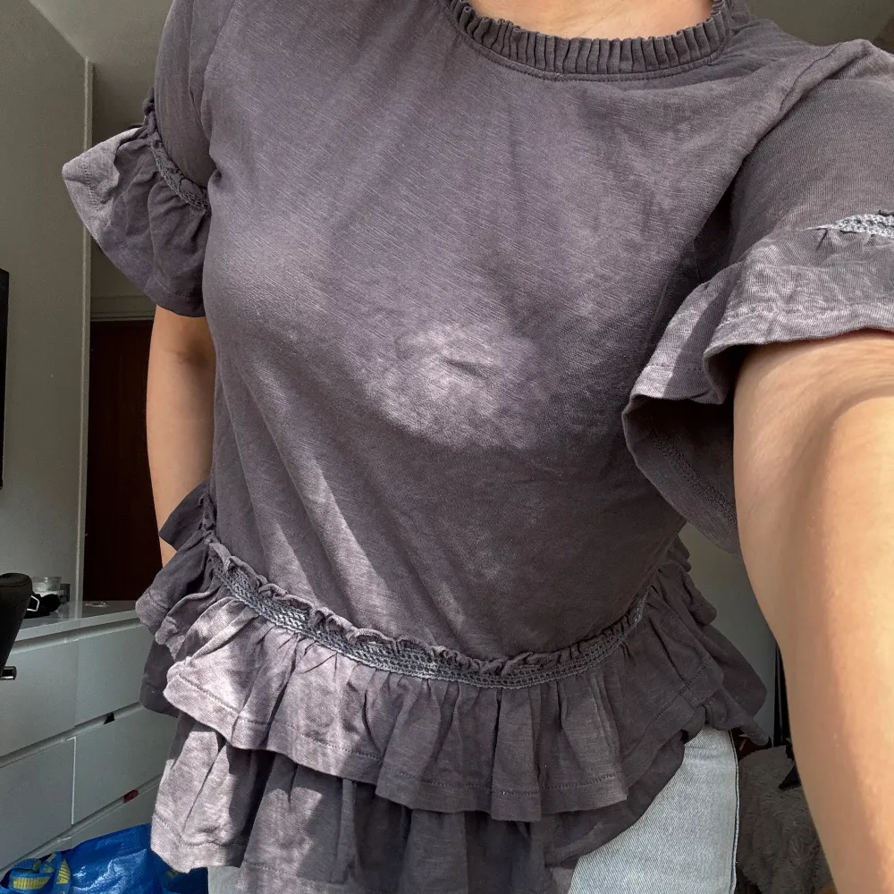 Supersöt grå topp från Odd Molly med volangdetaljer både vid ärmslut och nederkant. Toppen har korta ärmar och rund halsringning. Perfekt för dig som gillar romantiska och feminina detaljer.. Yläosat.