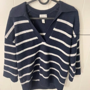 Marinblå  stickad tröja  - Mysig marinblå stickad tröja från H&M med vita horisontella ränder. Tröjan har v-ringning, krage och långa ärmar. Perfekt för lager-på-lager och passar till många olika stilar.