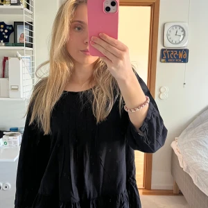 Svart blus med volangdetalj - Säljer en stilren svart blus med volangdetalj vid nederkanten. Blusen har trekvartsärmar och en rund halsringning. Perfekt för en chic och avslappnad look.