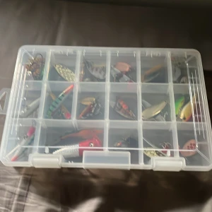 Fiskedrag (alla drag inkluderade) - Säljer en praktisk plastlåda fylld med olika fiskedrag. Lådan har flera fack och innehåller drag i olika färger och former, inklusive röda, gröna och silverfärgade. Perfekt för fiskeentusiasten som vill ha ett varierat utbud av beten.